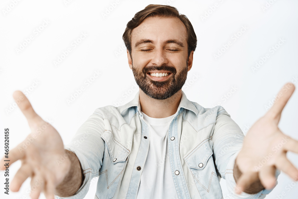 Smiling bearded guy close eyes, reaching to hold something, receiving in hands, standing over white background
