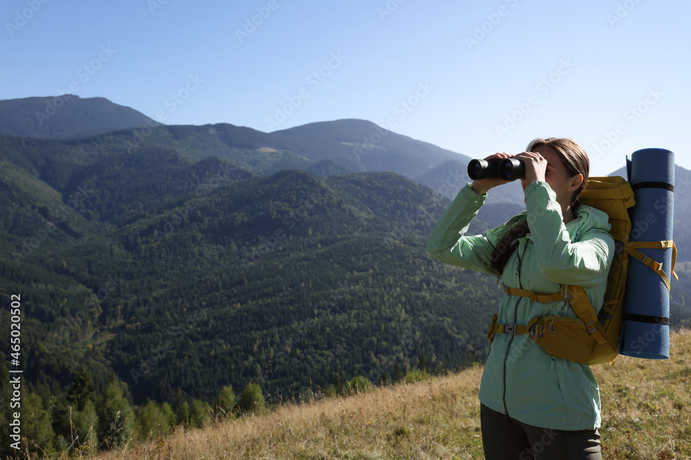 Tourist with backpack and sleeping pad looking through binoculars in mountains