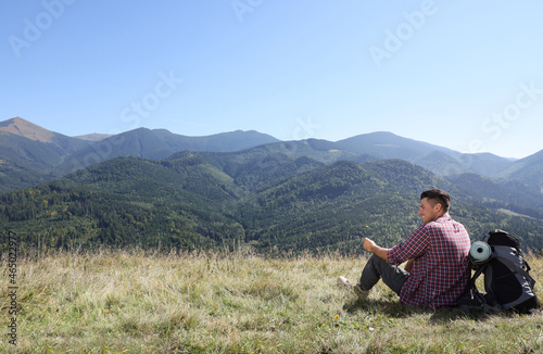 Tourist with backpack sitting on ground and enjoying view in mountains
