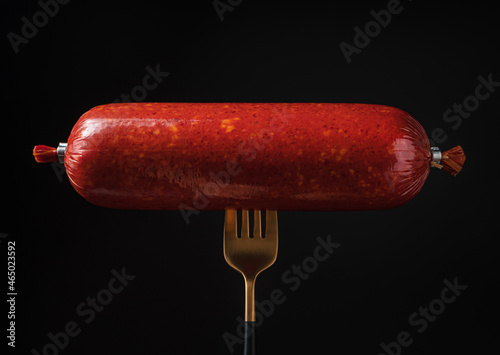 Smoked sausage on a fork on a black background.