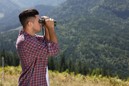 Man looking through binoculars in mountains on sunny day