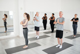Group of people with instructor meditating together with eyes closed during yoga class in studio