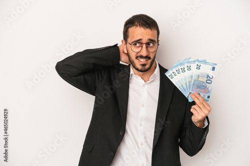 Young caucasian business man holding banknotes isolated on white background touching back of head, thinking and making a choice.