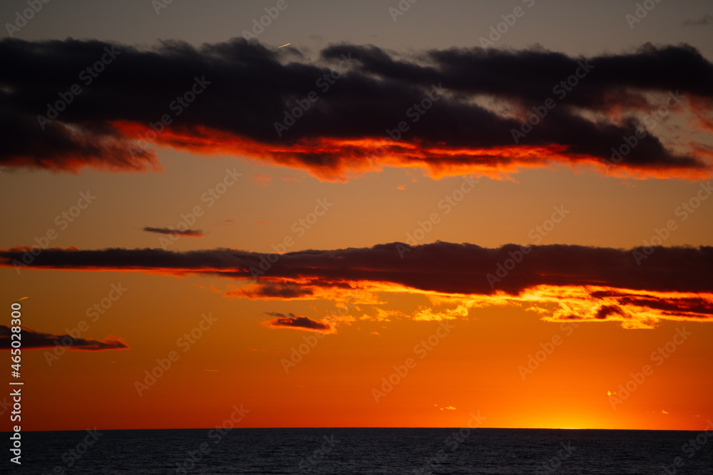 Fototapeta premium golden light of sunset falling below the horizon with orange glow reflecting off clouds sun setting over Lake Ontario Canada horizontal format room for type