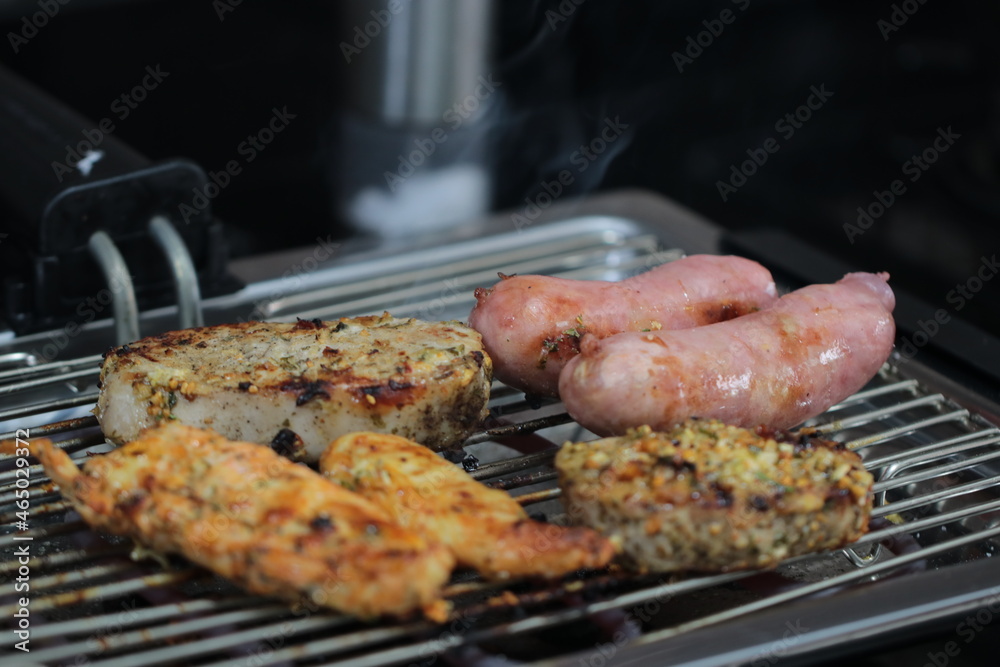 Churrasqueira elétrica com carnes sobre grelha, linguiça, frango e pernil de porco