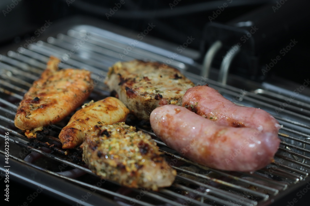 Churrasqueira elétrica com carnes sobre grelha, linguiça, frango e pernil de porco Churrasqueira elétrica com carnes sobre grelha, linguiça, frango e pernil de porco