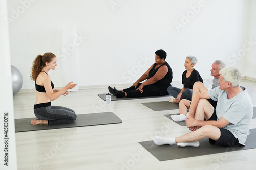 Senior people sitting on the floor and listening to the trainer during sports training in the studio