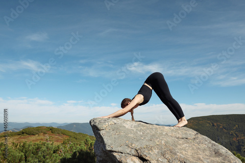 Beautiful young woman practicing yoga on rock in mountains