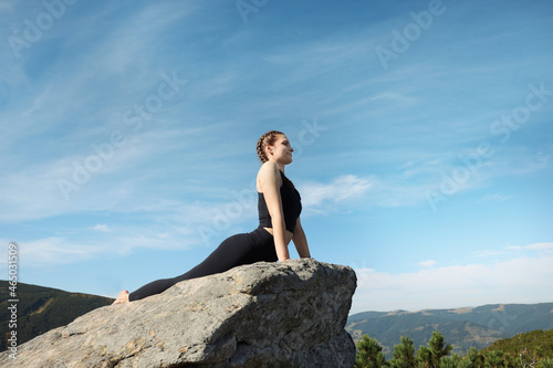 Beautiful young woman practicing yoga on rock in mountains