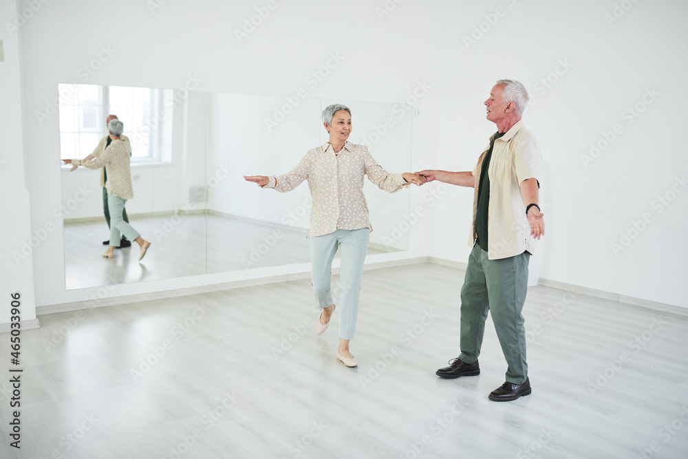 Happy senior couple learning to dance in front of the big mirror in dance studio Happy senior couple learning to dance in front of the big mirror in dance studio