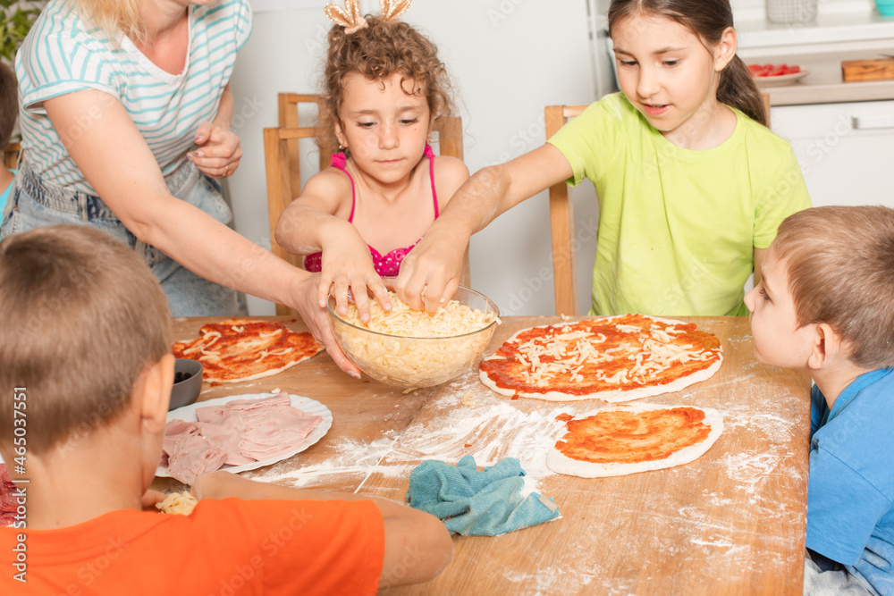 The group of kids with a teacher are preparing pizza