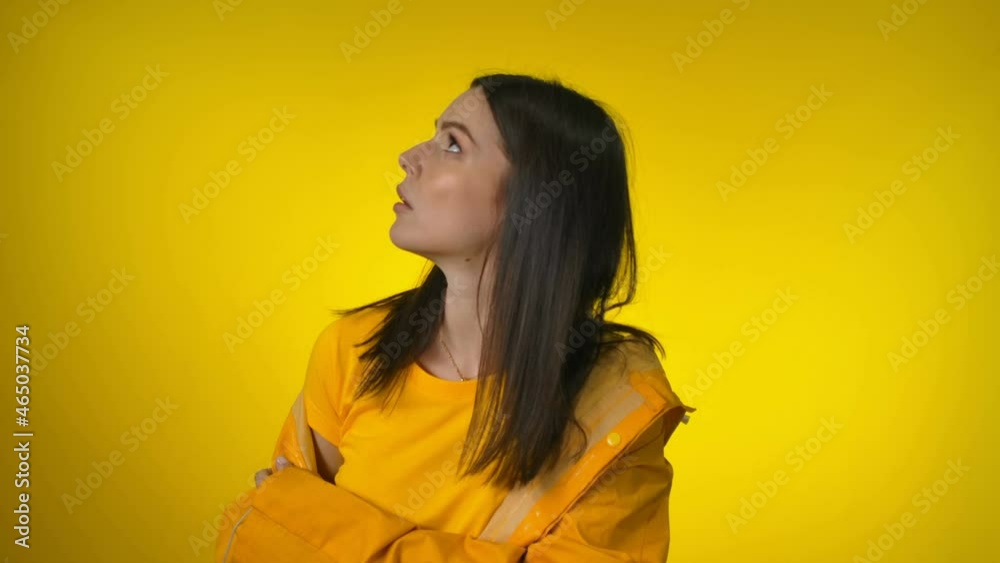 Happy attractive woman in a bright yellow raincoat is worried and looking up Happy attractive woman in a bright yellow raincoat is worried and looking up