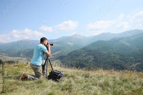 Professional photographer taking picture with modern camera in mountains. Space for text photo