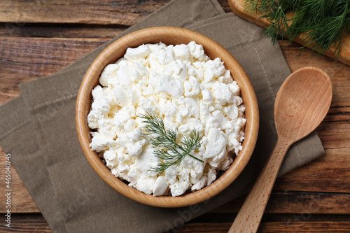 Fresh cottage cheese with dill in wooden bowl and spoon on table, flat lay