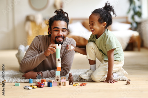 Happy african american family father and child son laughing while playing toys together at home