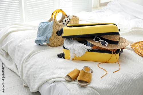 Open suitcase full of clothes, shoes and summer accessories on bed in room