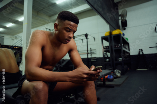 Young African American male looking at his phone to reply to an online message. male personal trainer looking at his phone while sitting down in the gym. High quality photo 