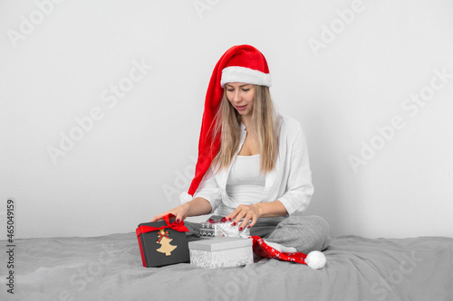 Young woman in Santa's hat openes Christmas presents sitting on bed. White background. photo