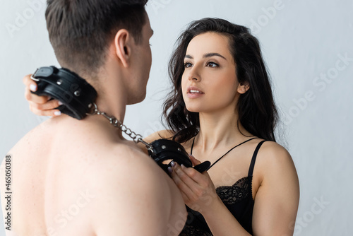 sexy and dominant woman holding leather handcuffs near shirtless man photo
