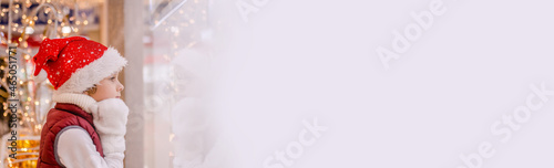 Boys in Santas hat looks into the store through the window in market. Copy space, space for text, banner