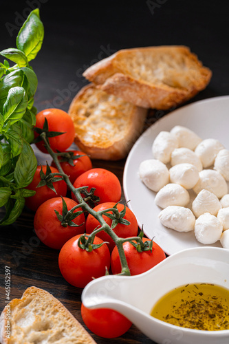 fresh ripe basil leaves with aromatic tomatoes and italian mozzarella, on the table. next to bruschetta and olive oil with Provencal herbs
