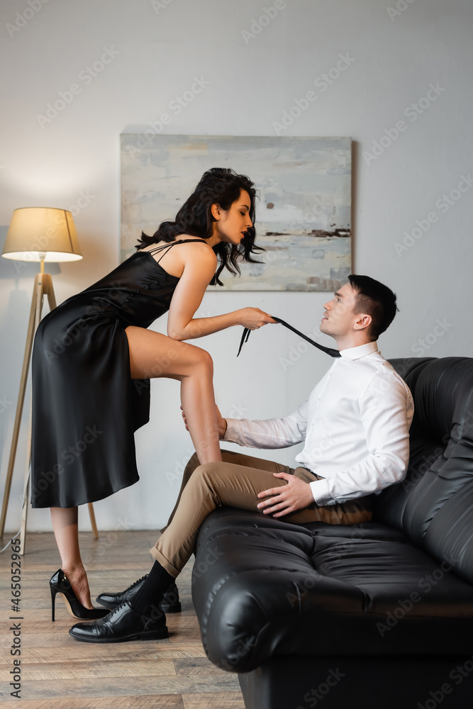 side view of sexy woman in black slip dress pulling tie while seducing man  on sofa Stock Photo | Adobe Stock