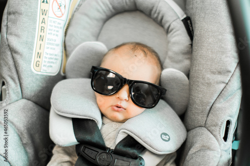 newborn baby boy wearing sunglasses in a gray carseat photo