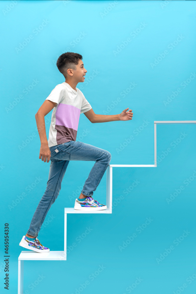 Young smiling teen boy climbs the development ladder against blue background. Education concept
