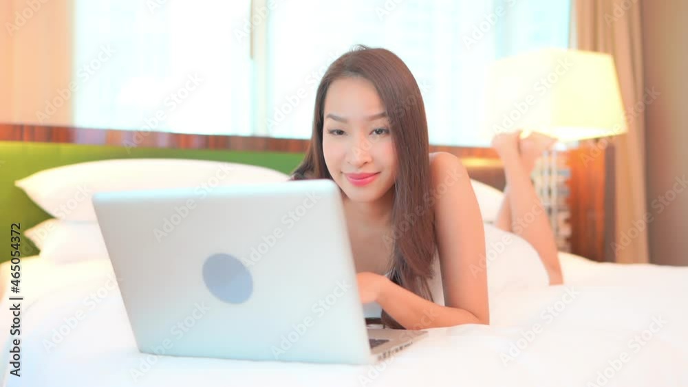 Young Asian woman freelancer lying on the bed at home and working on the laptop computer. Feeling excited of hearing unbelievable news, celebrating success or win good luck concept. Young Asian woman freelancer lying on the bed at home and working on the laptop computer. Feeling excited of hearing unbelievable news, celebrating success or win good luck concept.