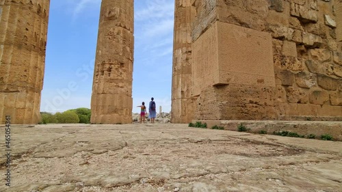 First-person ground level view toward mother and child tourists at Greek temple colonnade at Selinunte archaeological park in Sicily, Italy. Slow-motion photo
