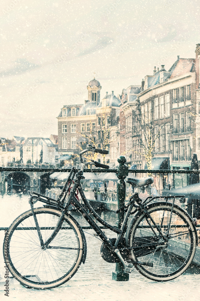 Winter view with snowfall of the Dutch Nieuwe Rijn canal with bridge and bicycle in the city center of Leiden