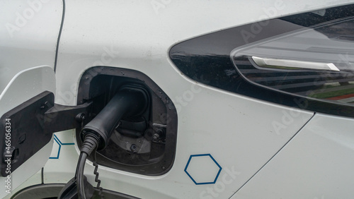 Close-up view of power supply plugged into an electric car being charged. White electric car charging.