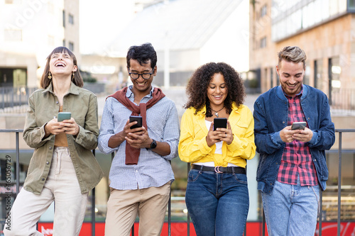 Multiracial friends laughing using smartphone in the university district of the city - Young people addicted by mobile smart phones - Technology concept with always connected gen z and millennials photo