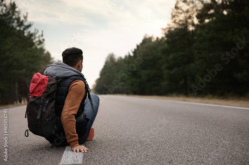 Man with backpack sitting on road near forest  back view