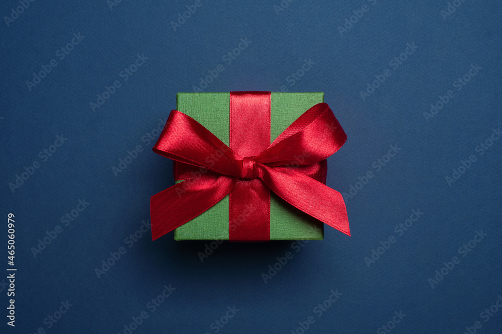 Christmas green gift box decorated with red satin bow on blue background