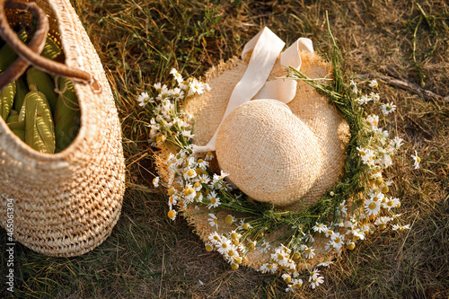 A straw hat decorated with a wreath of daisies. Bag of corn cobs