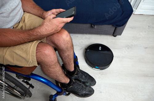 unrecognizable man in wheelchair controlling cleaning robot from smart phone
