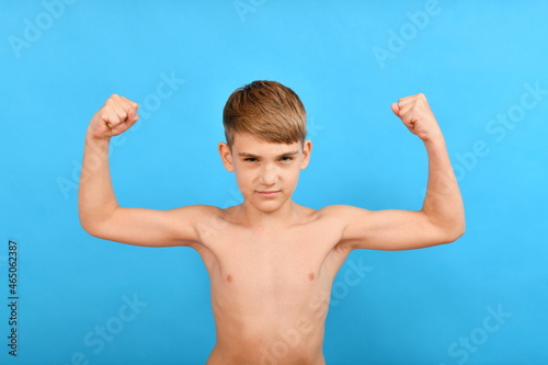 A small thin boy without muscles raised his arms to the top and shows biceps. Lean and skinny bodybuilder.