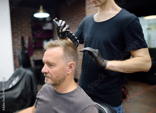 Stylist making hairstyle for person in barbershop. Hairdresser is cutting hair of handsome bearded mature man in salon. Services of a professional stylist.