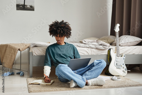 Fotografija Full length portrait of teenage African-American student sitting on floor at hom
