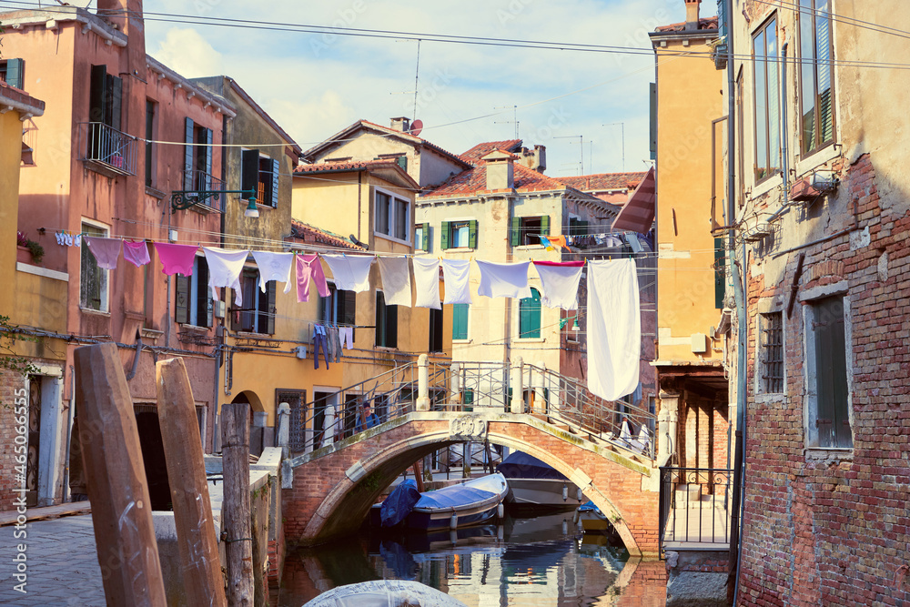 Washing lines across canal in Venice, Italy. Laundry hanging on a clothes line between city buildings and above bridge. Clothes lines between windows of old brick houses in Venice.