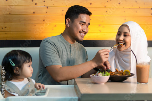 Photography Young malay couple at the restaurant smiling and enjoying their food