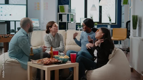 Cheerful coworkers playing guessing game with sticky notes on forehead after work for entertainment. Workmates enjoying fun activity with beer drinks, snacks and play after hours.