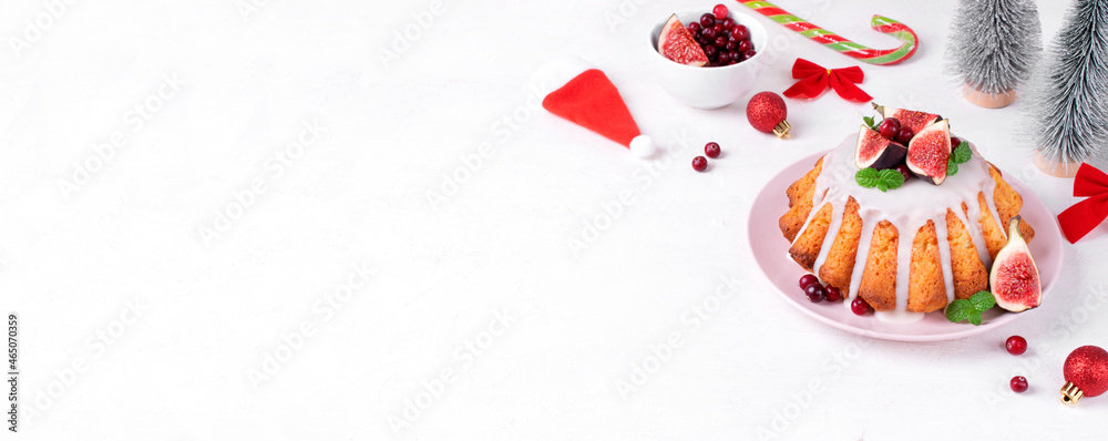 Web banner with Christmas cake topped with icing, figs, cranberry and mint on white table. Dessert in festive table setting. Template with copy space