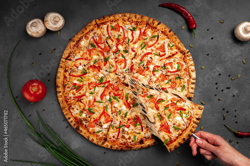 A woman's hand takes a slice of pizza with a spatula and the cheese stretches, top view.