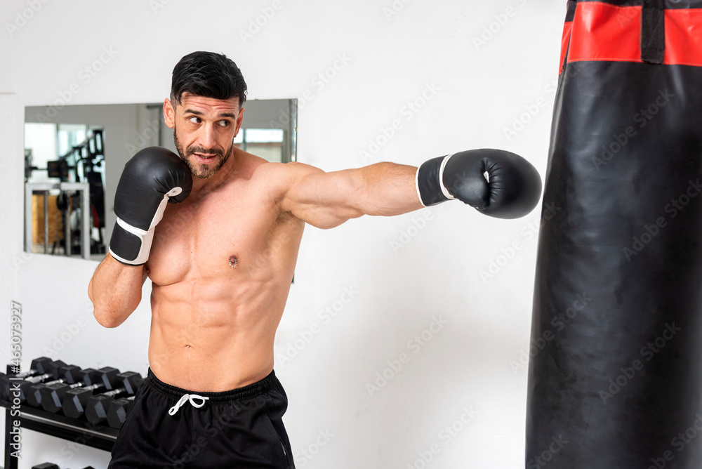 muscular young man, bare-chested, wearing boxing gloves training in gym