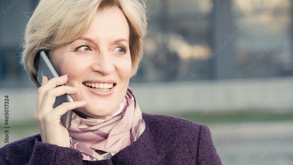 happy middle aged woman looking away while talking on smartphone outdoors.
