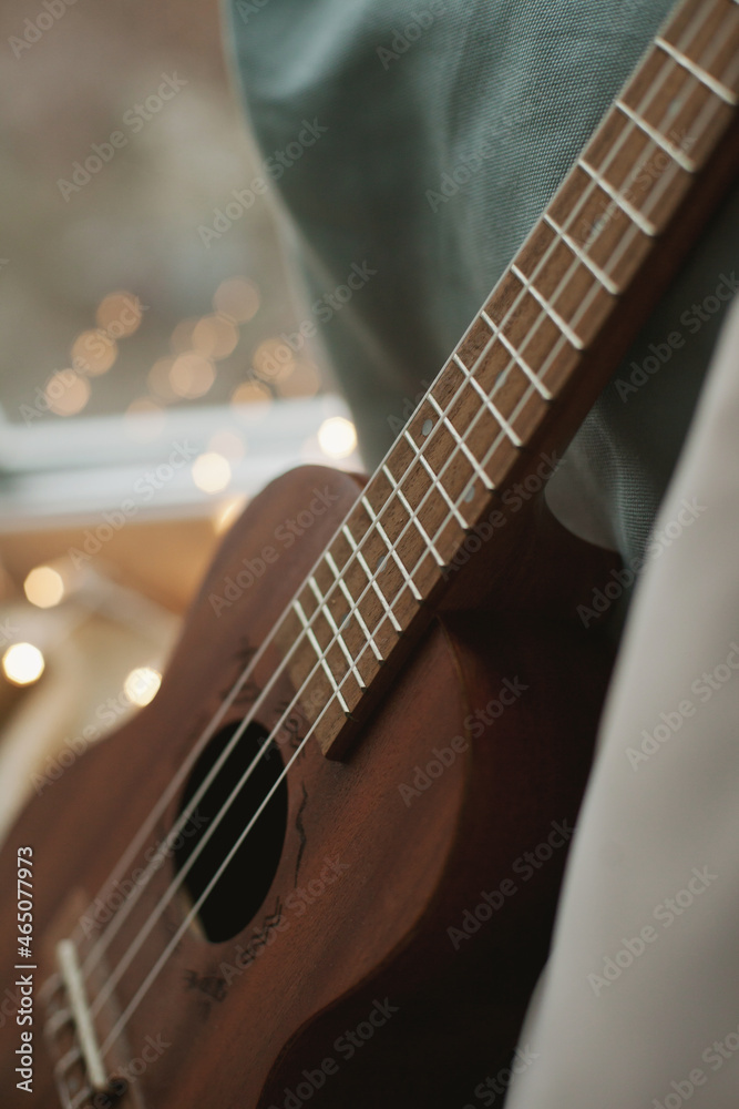 Fototapeta premium Ukulele on the windowsill with cozy pillows and lights at home closeup