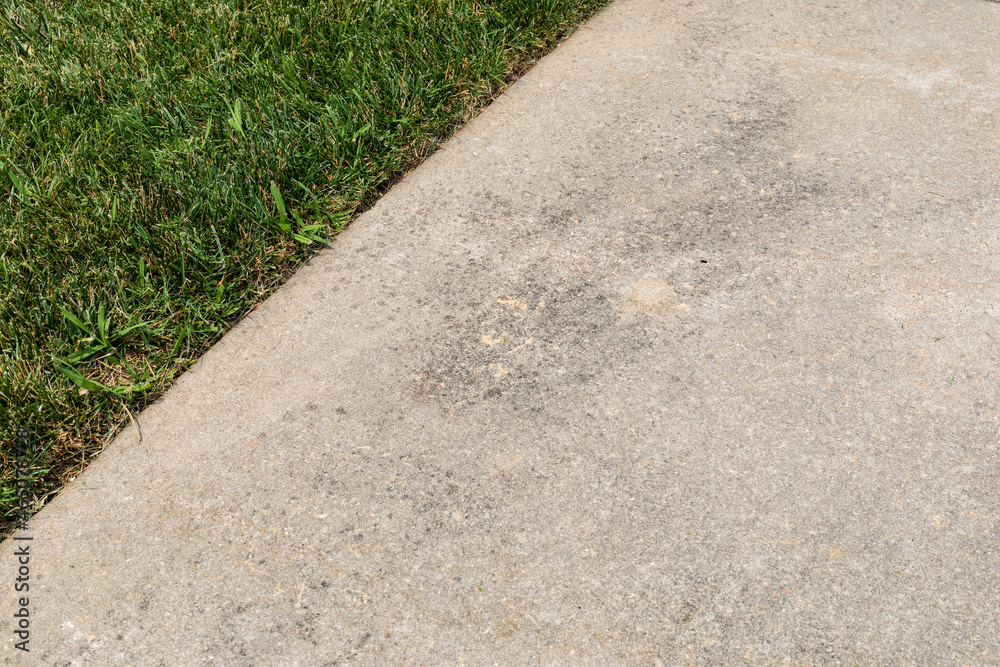 Concrete sidewalk with light staining set diagonally alongside green grass, well tended, horizontal aspect