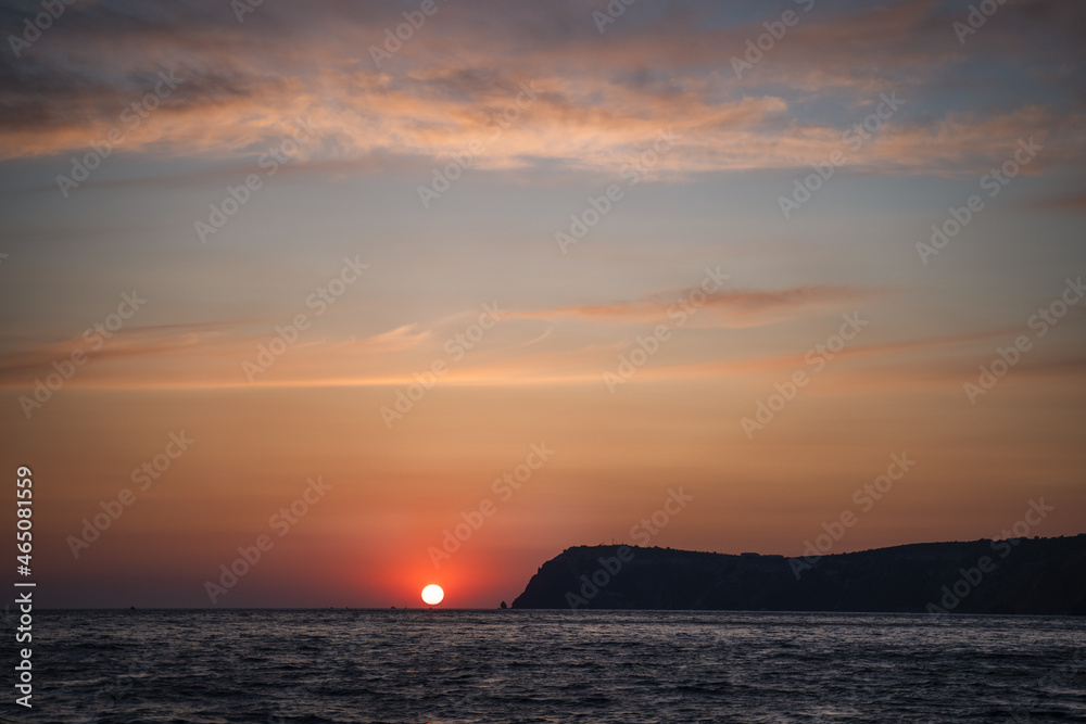 Dramatic Seascape over black sea surface during sunset, Silhouette of rocky volcanic cliff is lit by the warm sunset. Copy space. Never-ending beauty of nature